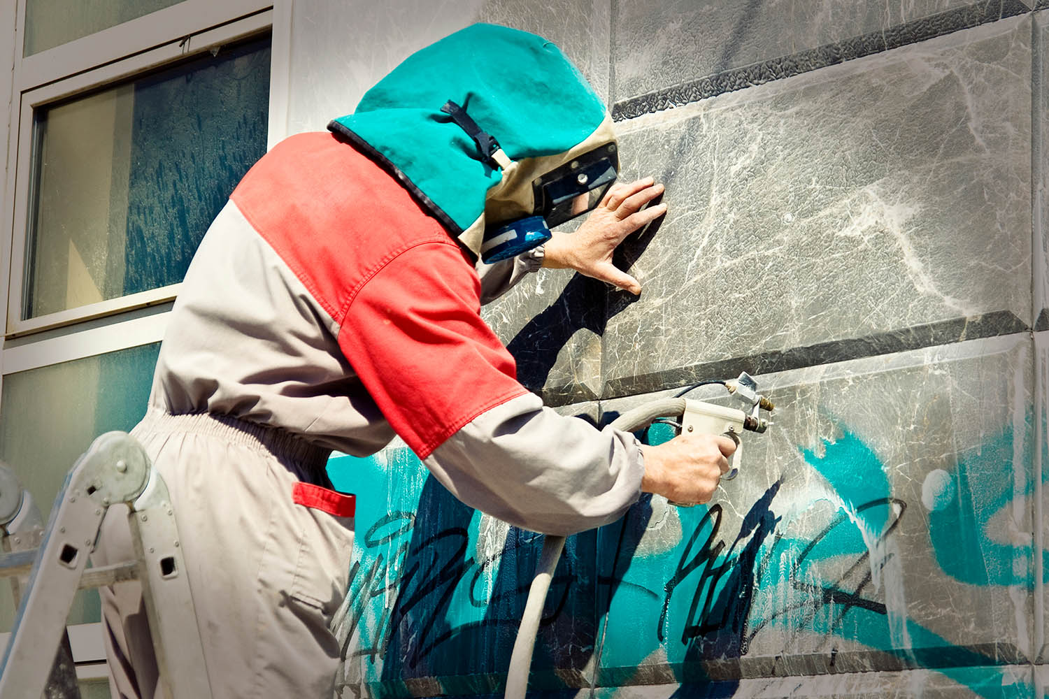 Man wearing a complete PPE and cleaning a vandalized wall