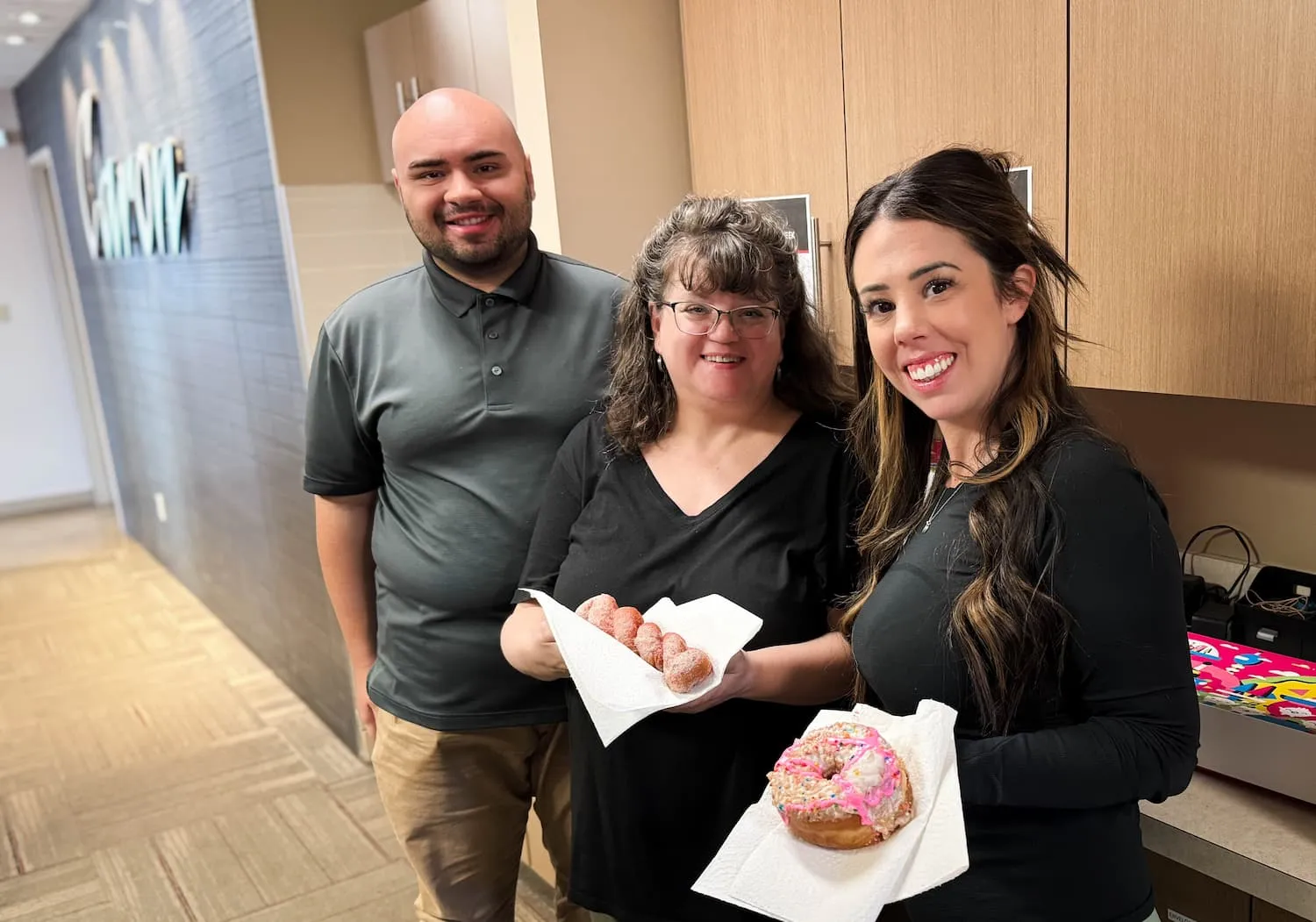Three people smiling in the Caron office, holding desserts