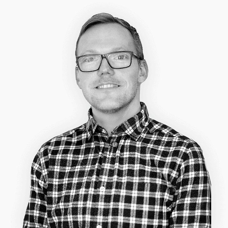 Man with short hair and glasses smiling, wearing a black and white plaid button-up shirt.