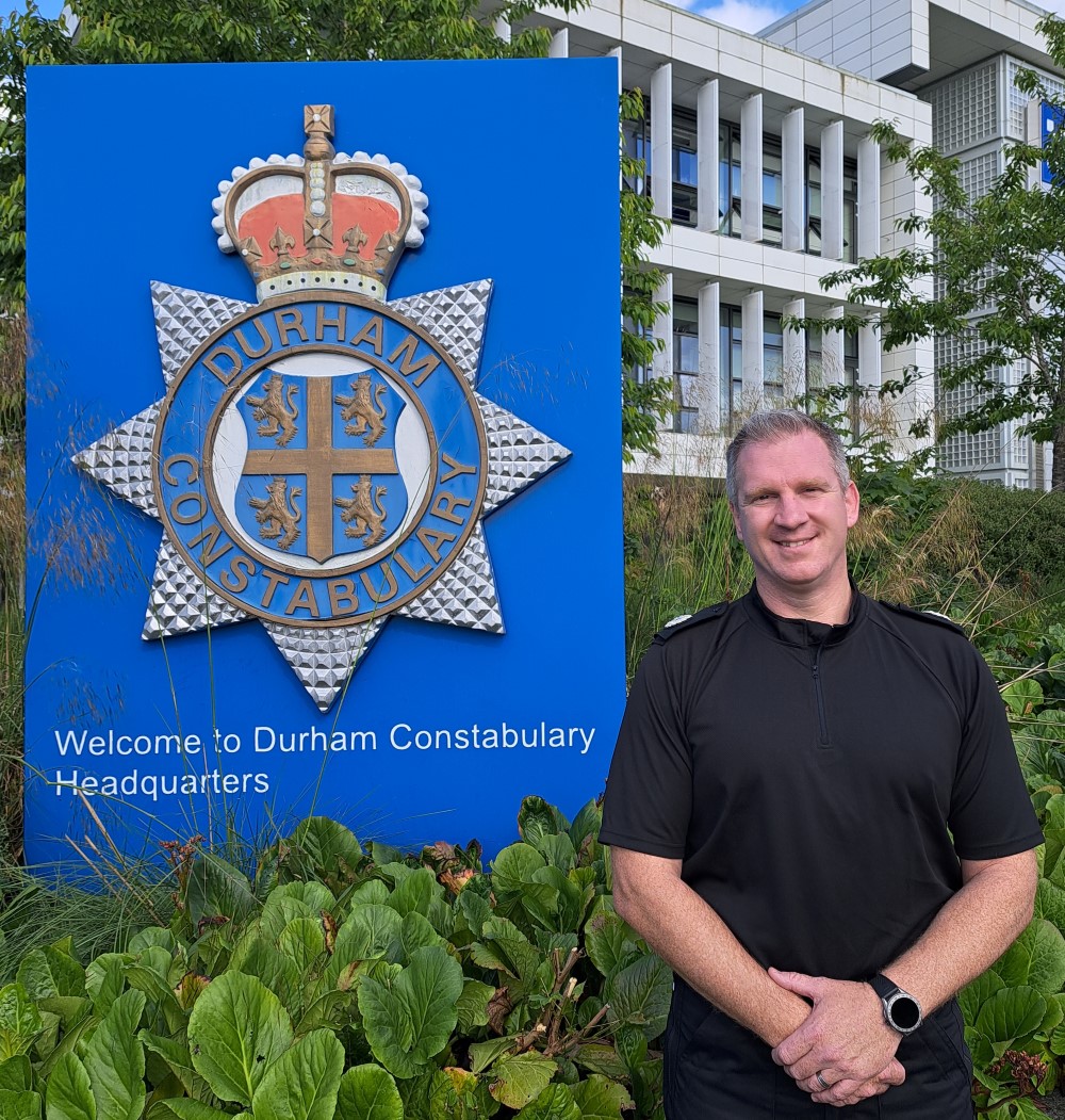 Assistant Chief Constable Jon McAdams standing next to Durham Constabulary badge.