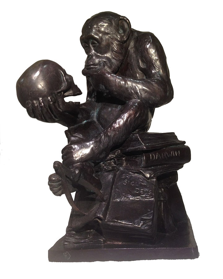 A bronze statue of a monkey sitting on books, holding a human skull and looking at it thoughtfully; the name "Darwin" is visible on one book.
