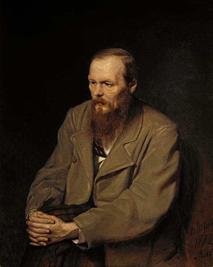 Seated man with a beard wearing a brown coat and clasping his hands