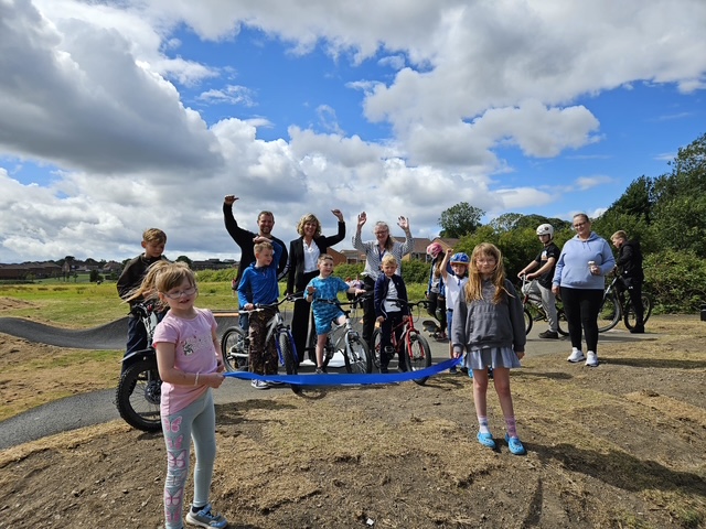 A group of children with bikes and adults celebrating by the track