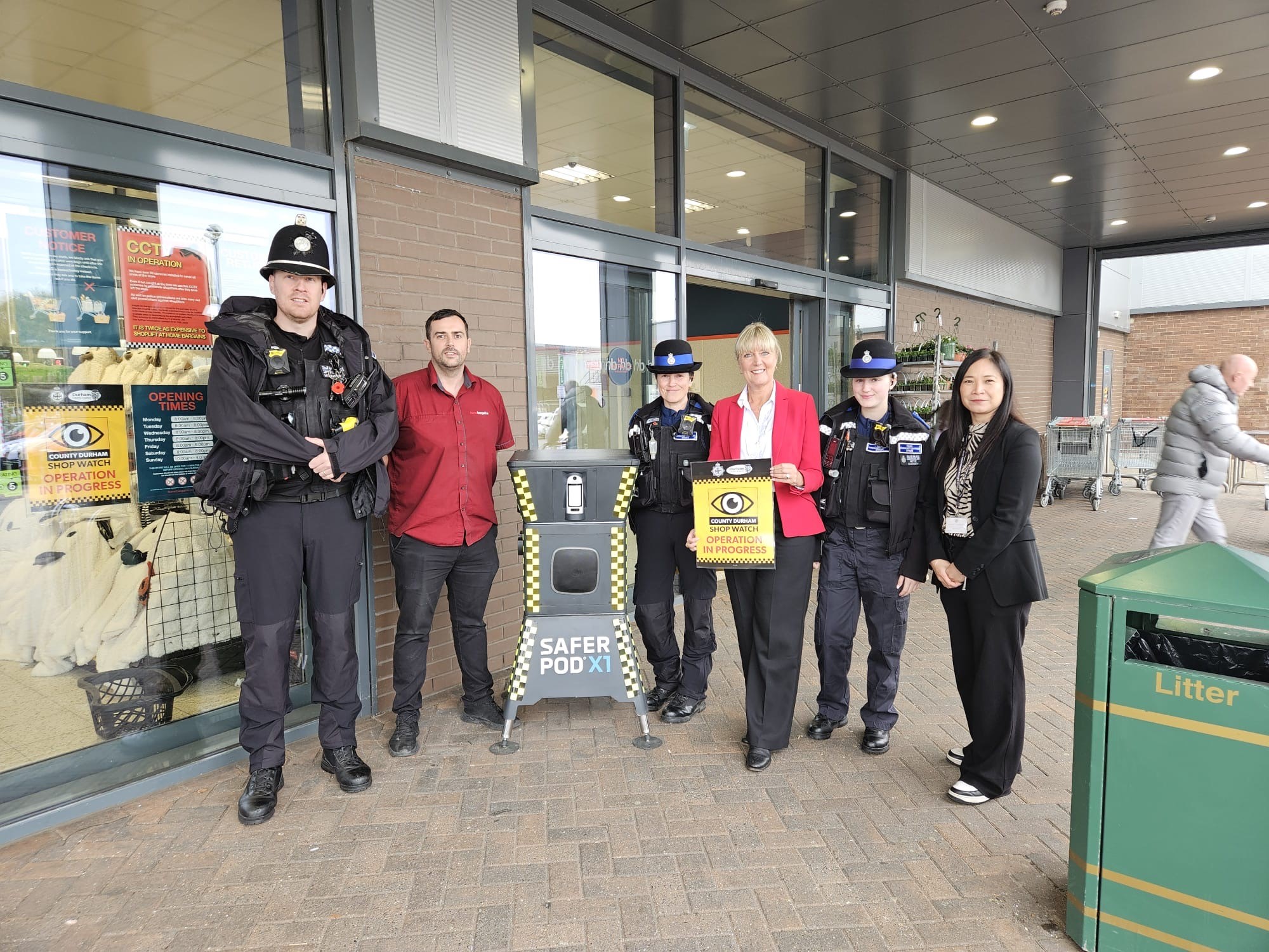 Group of people outside shop standing round a Safer Pod 