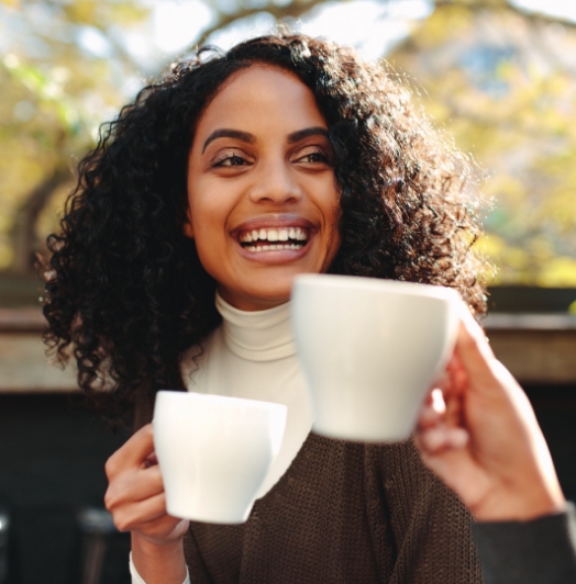 happy women drinking coffee out of white mugs with friend
