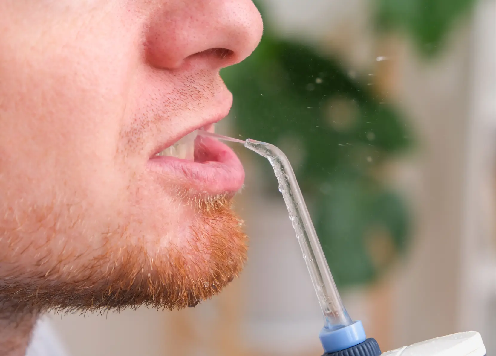 A young man is using a water flosser as part of their oral care routine.