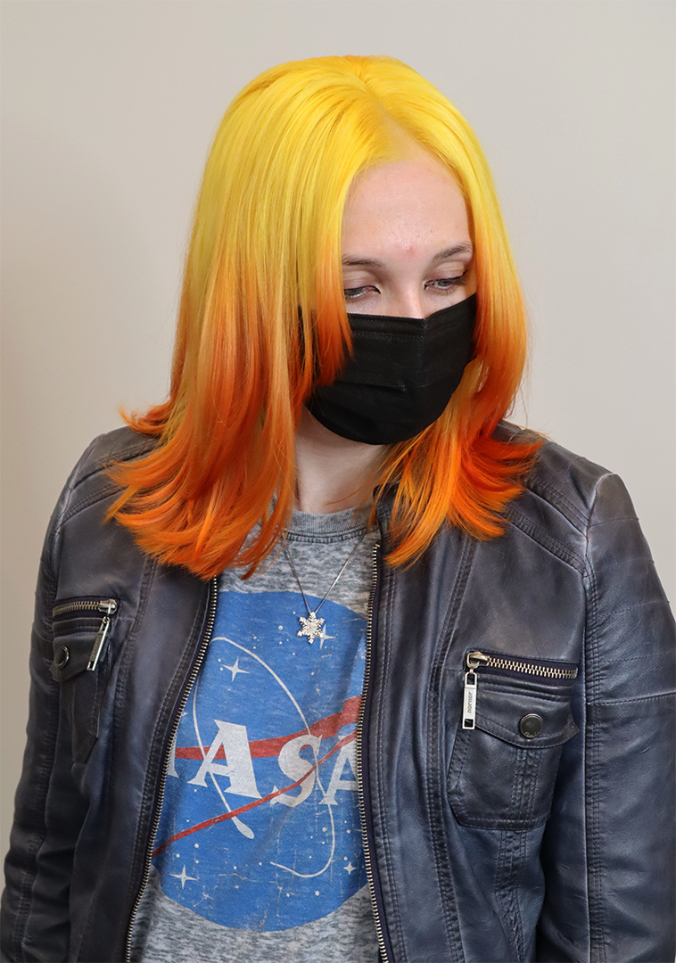 Hair salon client wearing a face mask. Her hair is yellow on top, fading to orange.