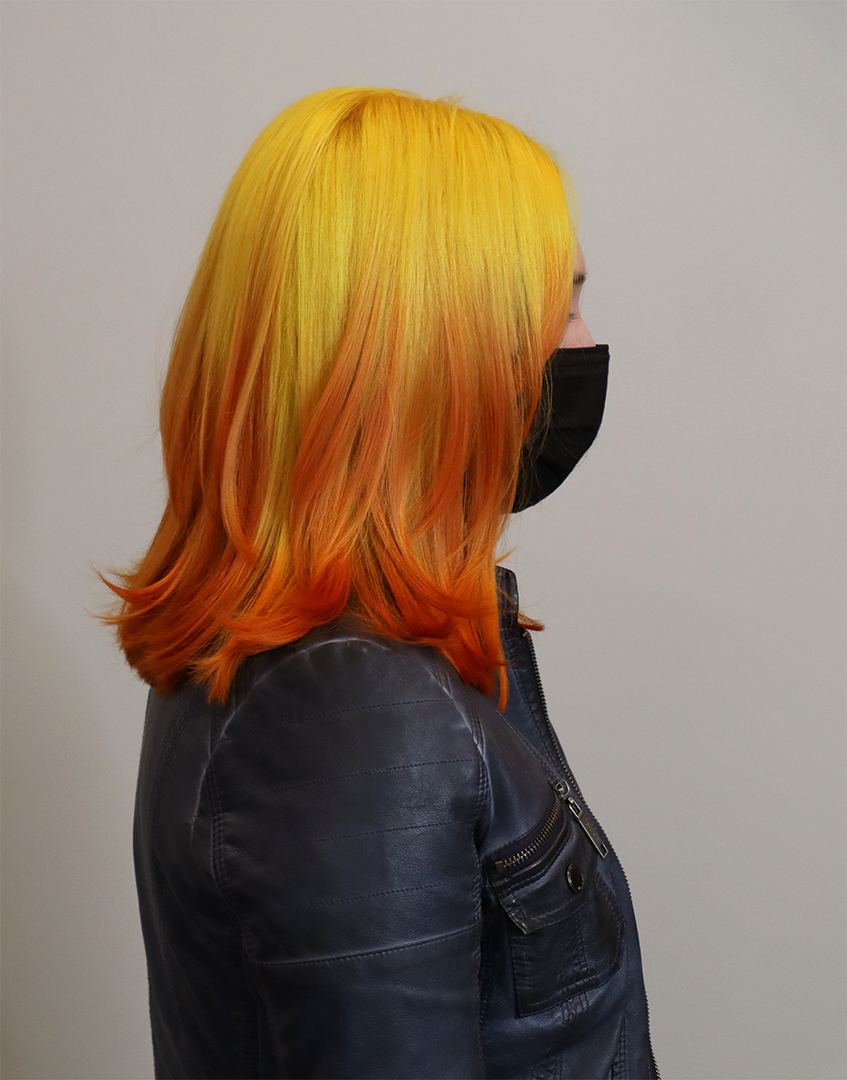 Side view of a hair salon client wearing a face mask. Her hair is yellow on top, fading to orange.
