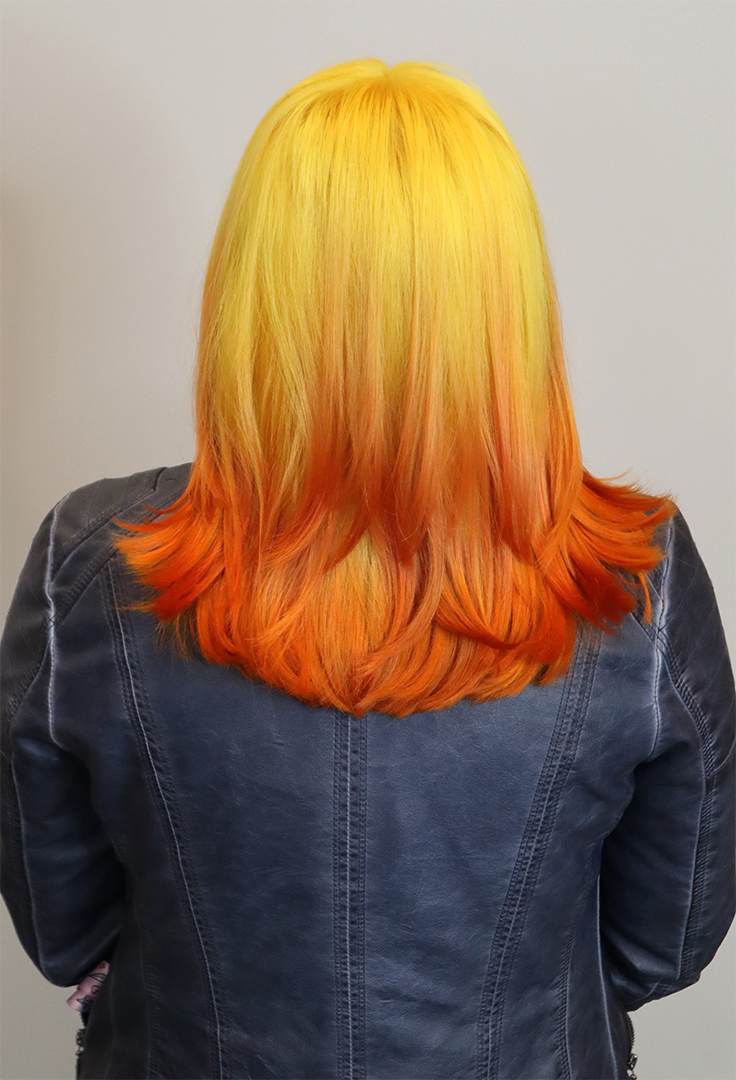 Back view of a hair salon client. Her hair is yellow on top, fading to orange.