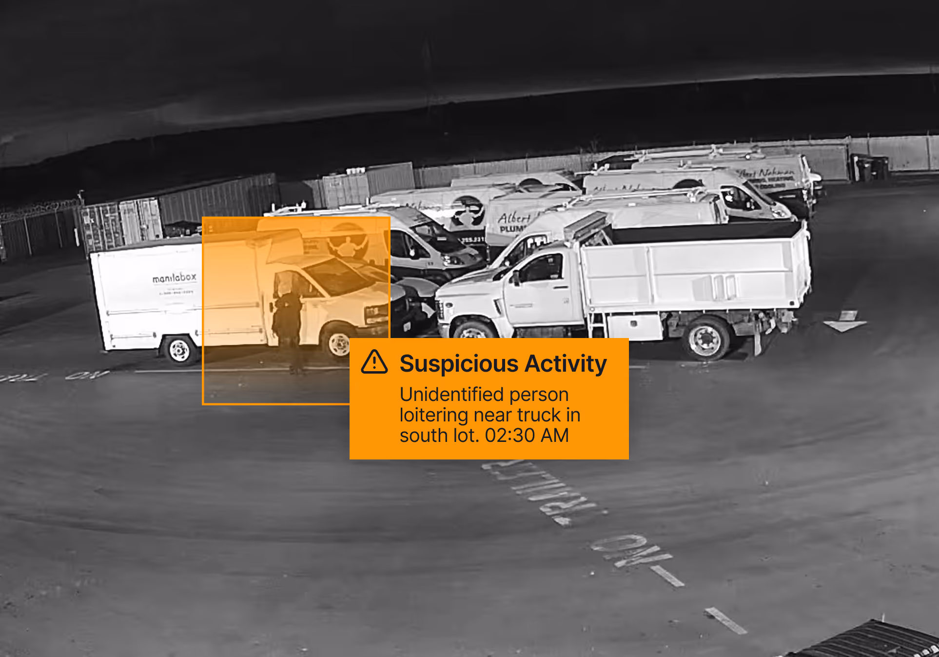 Nighttime surveillance image showing an unidentified person loitering near a white truck in a parking lot with multiple work vans.