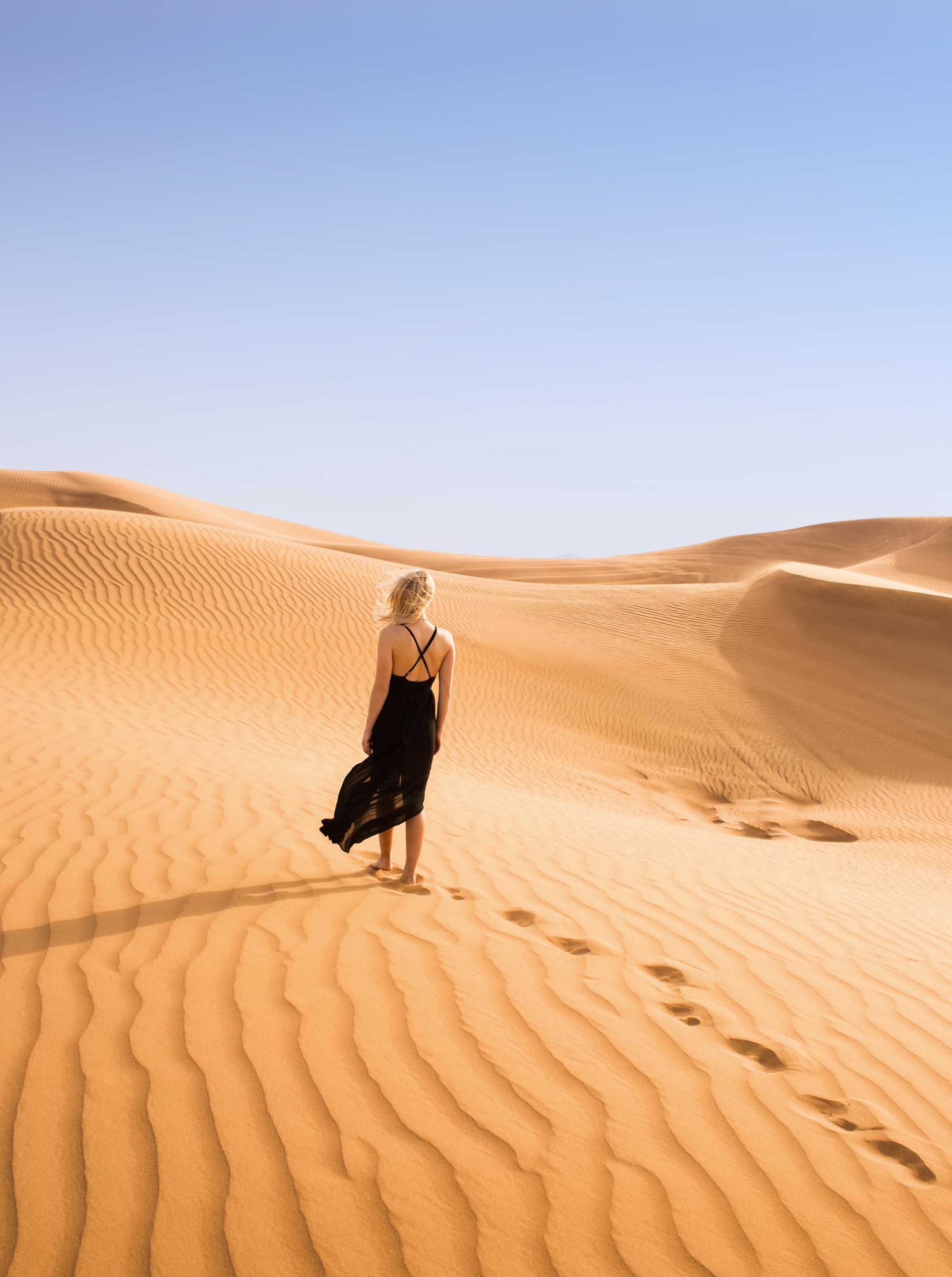 girl in black dress walks through the sand dunes of the desert in Dubai