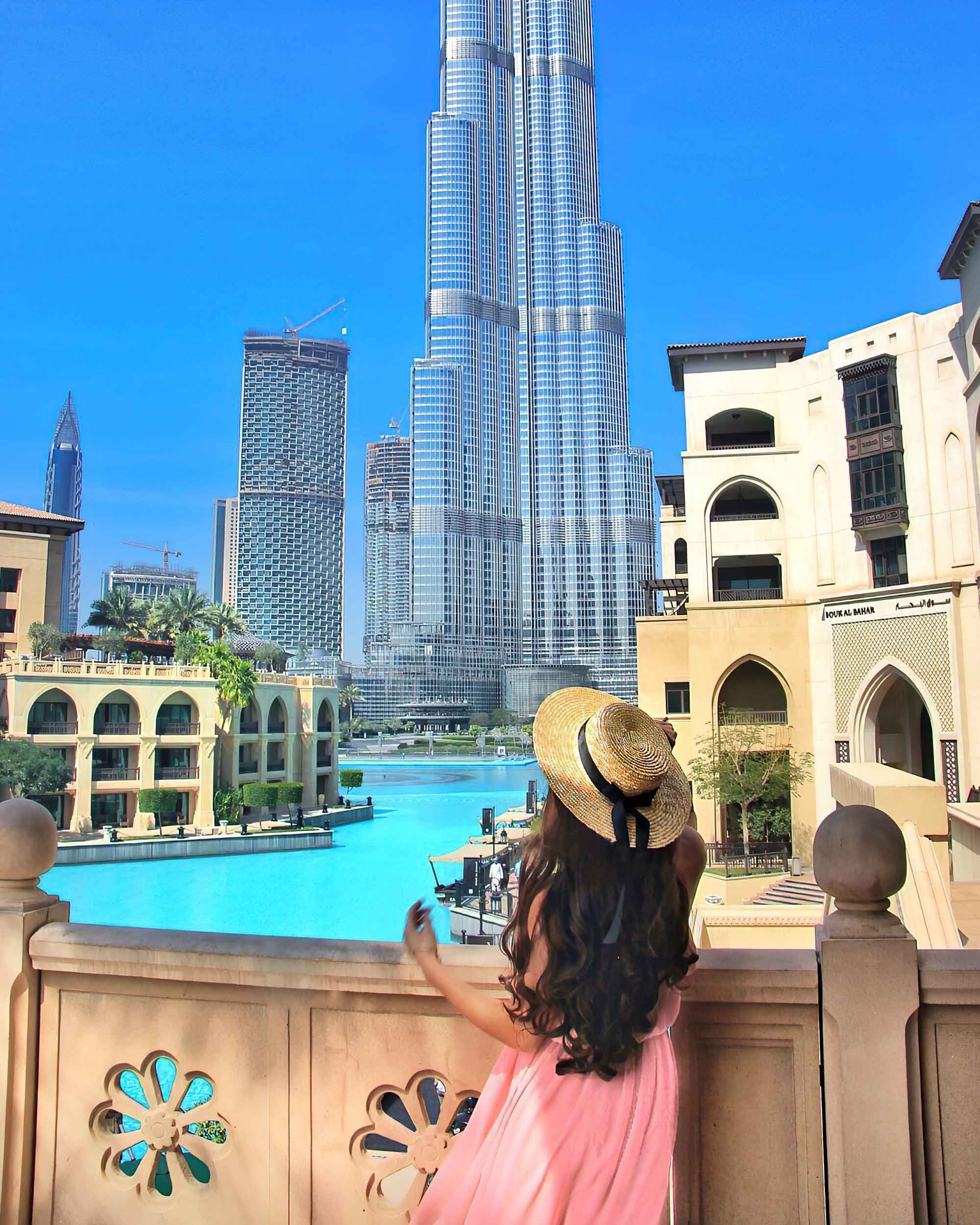 A girl in a pink dress and straw hat views the Burj Khalifa from across the decorative pools.