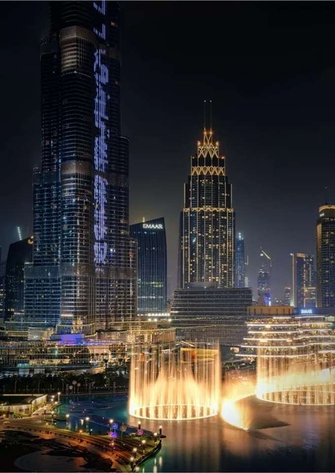 A view of a city at night with a fountain in the foreground.