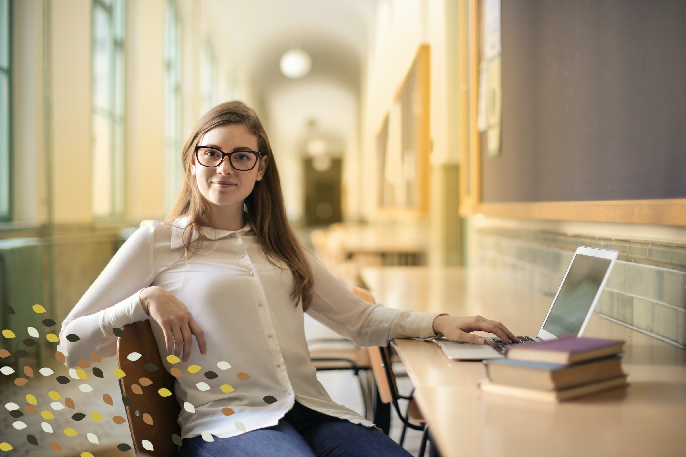A young woman with glasses sits in a long hallway. She looks away from her laptop and books wistfully, half-smiling at the photographer. She's a student
; she's happy with her studies.