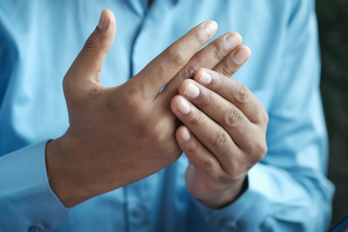A person in a blue shirt massaging their middle finger and ring finger