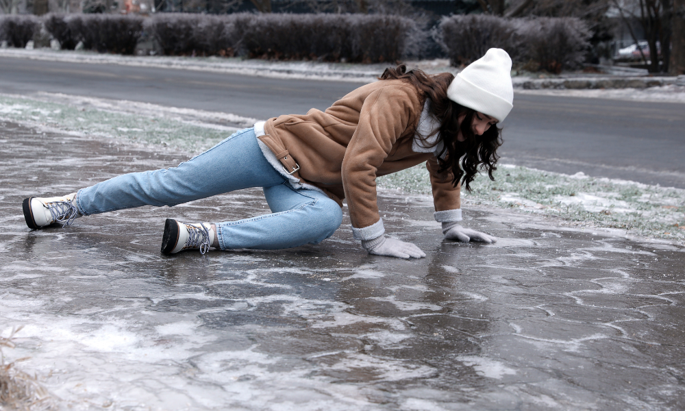 Woman wearing winter clothing slipping and falling on an icy sidewalk near a road.
