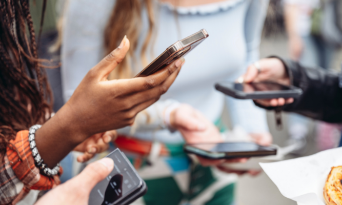 Close-up of a group of people holding and using smartphones outdoors, focusing on their hands and mobile devices.
