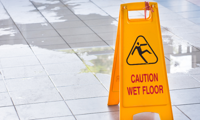 Yellow "Caution Wet Floor" sign placed on a shiny tiled floor with visible puddles of water around it.