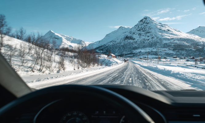 Driver's perspective of a snowy mountain road in Colorado, with clear skies, snow-covered peaks, and a winding road ahead, emphasizing winter driving conditions.