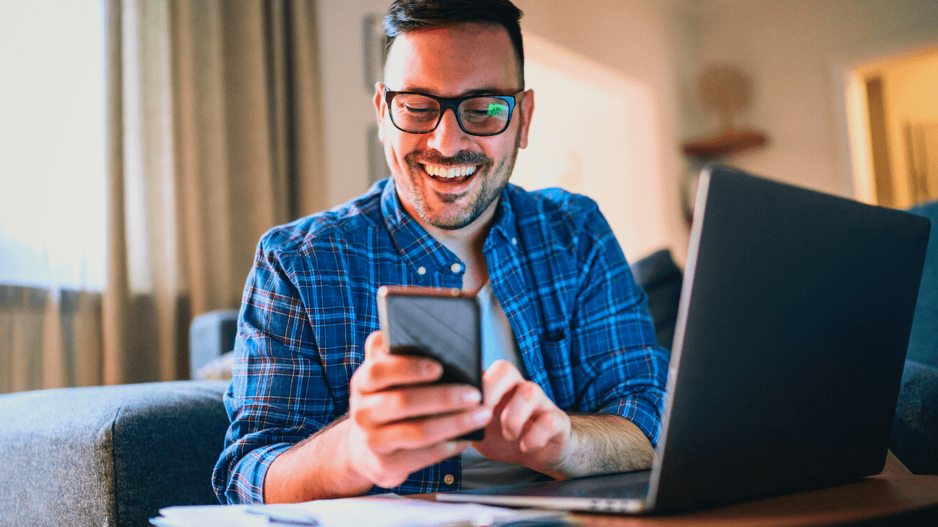 Homem feliz enquanto trabalha no computador e no celular