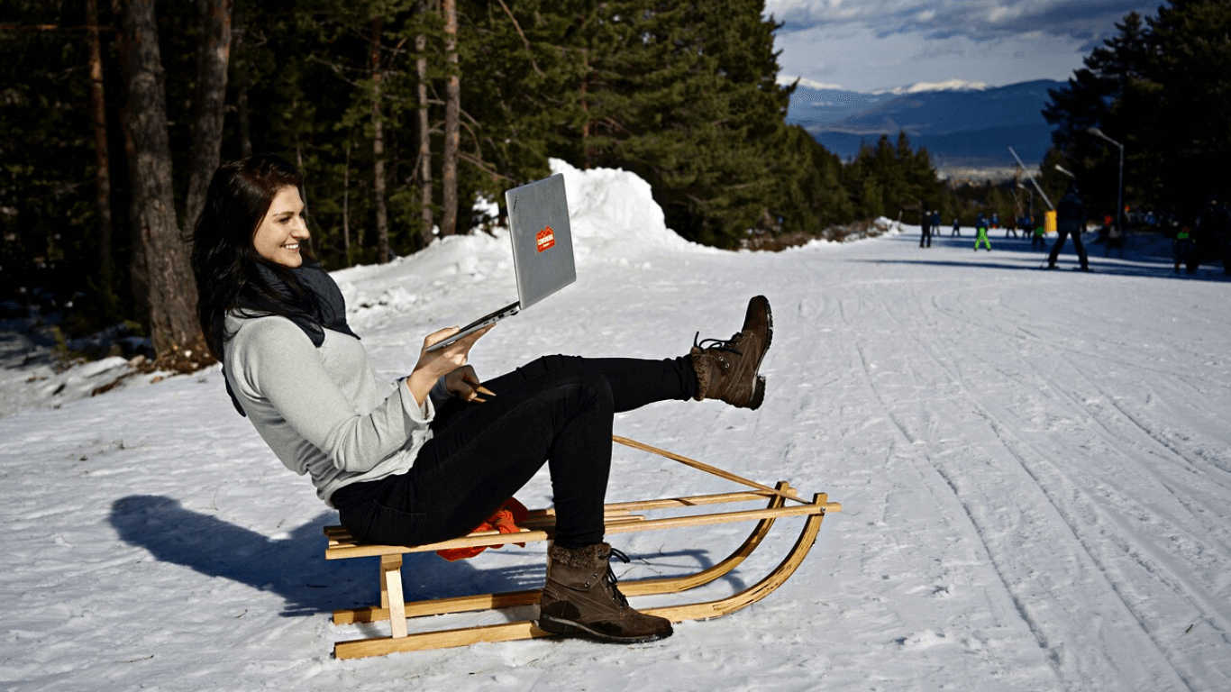 Mulher no meio da neve em um trenó de madeira com computador na mão
