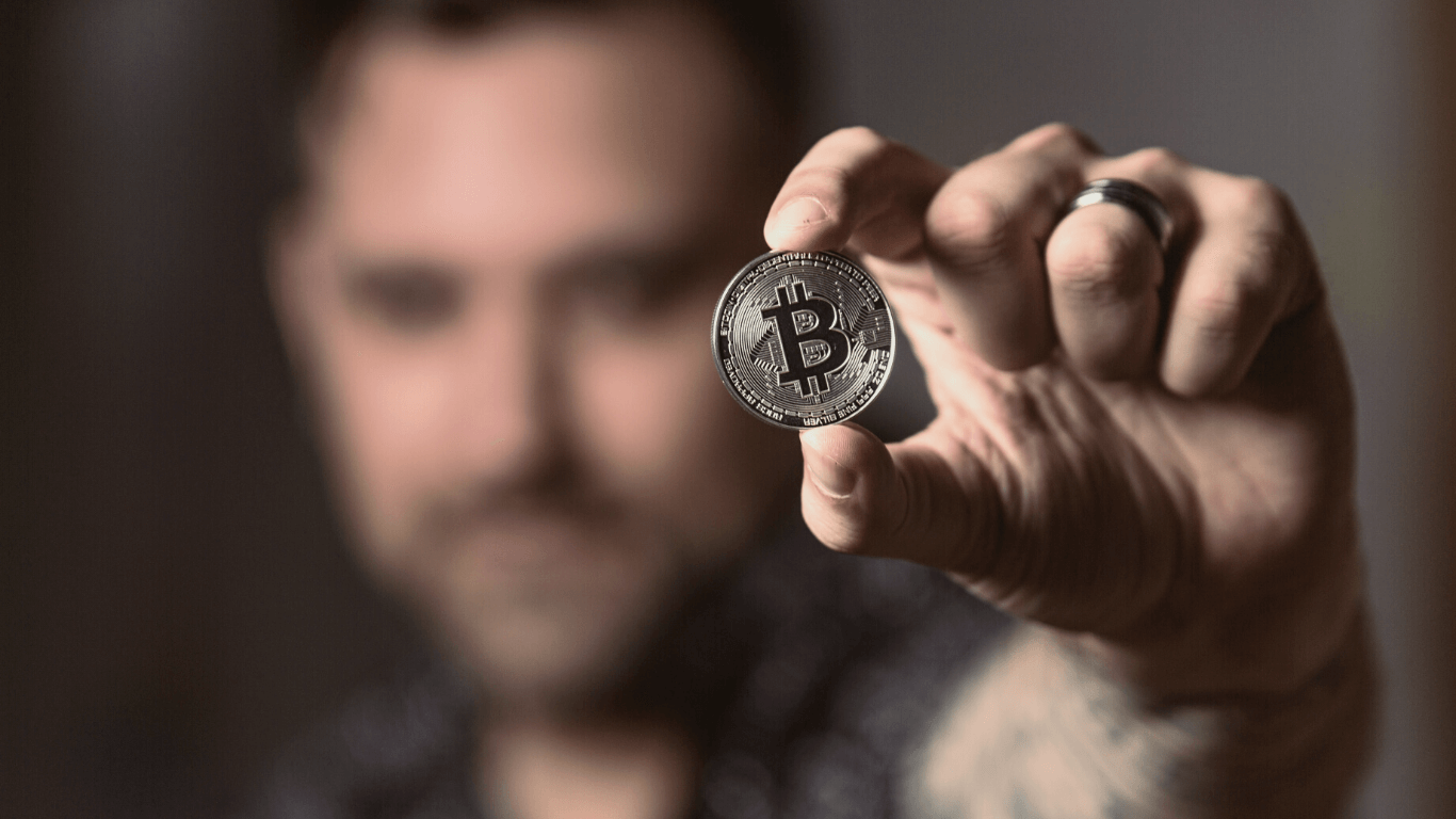 Homem egurando uma moeda de bitcoin nas mãos