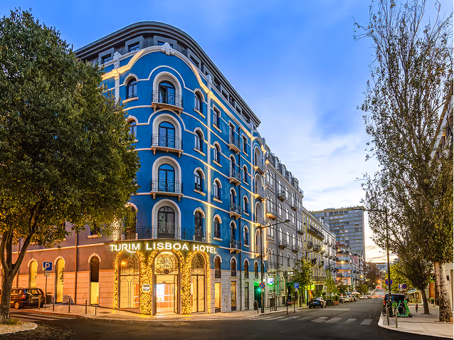 Turim Lisboa Hotel building with blue facade and illuminated entrance at a street corner in Lisbon at dusk.