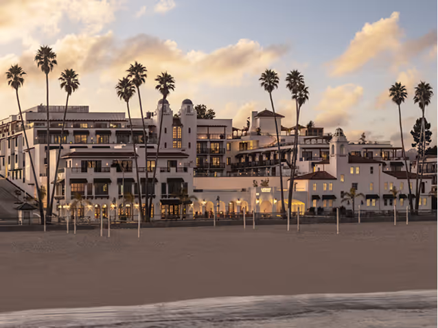 Large white Spanish-style beachfront hotel with tall palm trees under a partly cloudy evening sky.