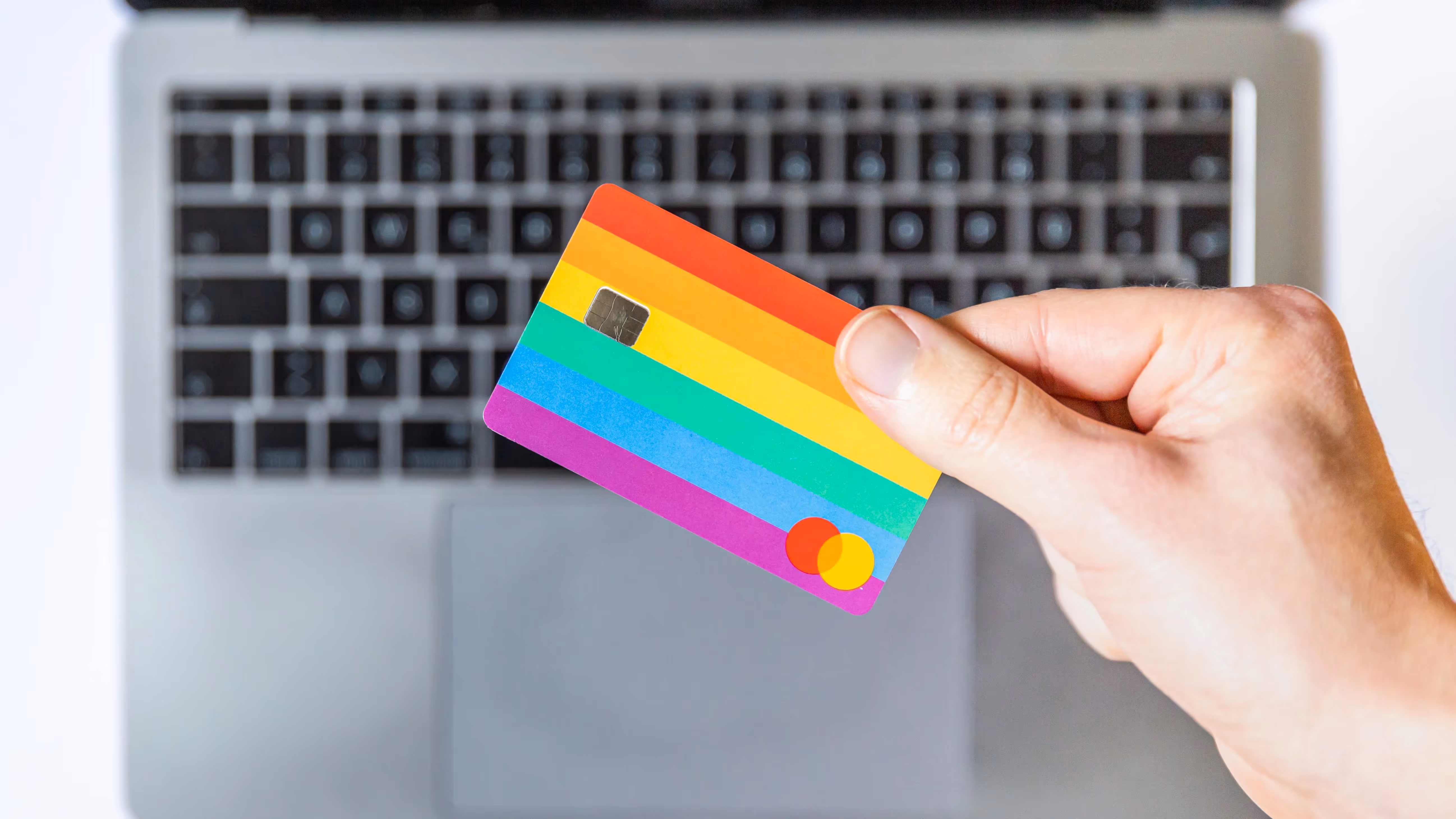 Carte de crédit colorée tenue au-dessus d'un clavier d'ordinateur portable.