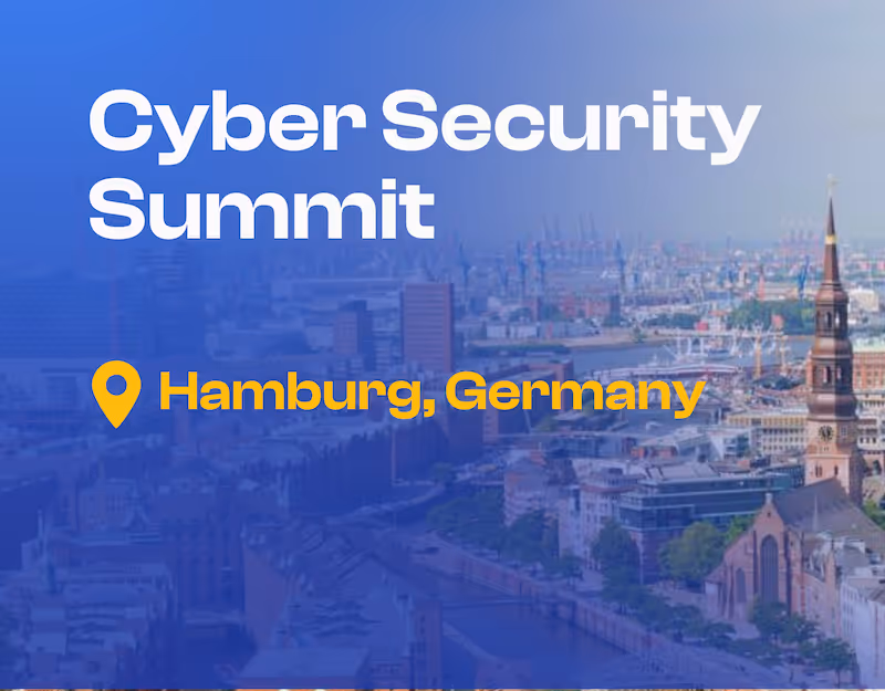 ドイツ・ハンブルクの空撮都市景観。運河沿いの歴史的な煉瓦造りの建物と前景に聳える教会の尖塔が特徴で、遠方には工業港が見える。画像には「サイバーセキュリティサミット」の文字と、黄色の場所ピンアイコンで「ドイツ・ハンブルク」と表示されている。