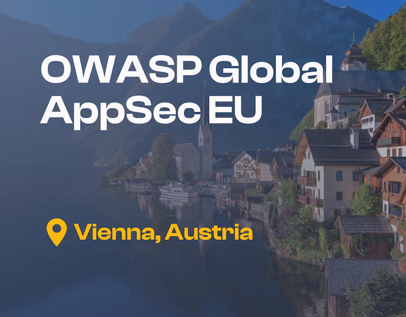 「OWASP Global AppSec EU」というテキストと「オーストリアのウィーン、オーストリア」と記されたロケーションピンが重なった湖畔の教会の尖塔と伝統的なアルプスの家々が特徴の、オーストリアのハルシュタットの美しい景色。