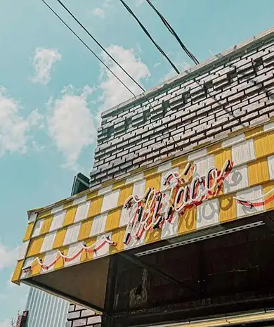 Tiki Taco location exterior on West 39th Street with a neon sign and yellow checkered awning.