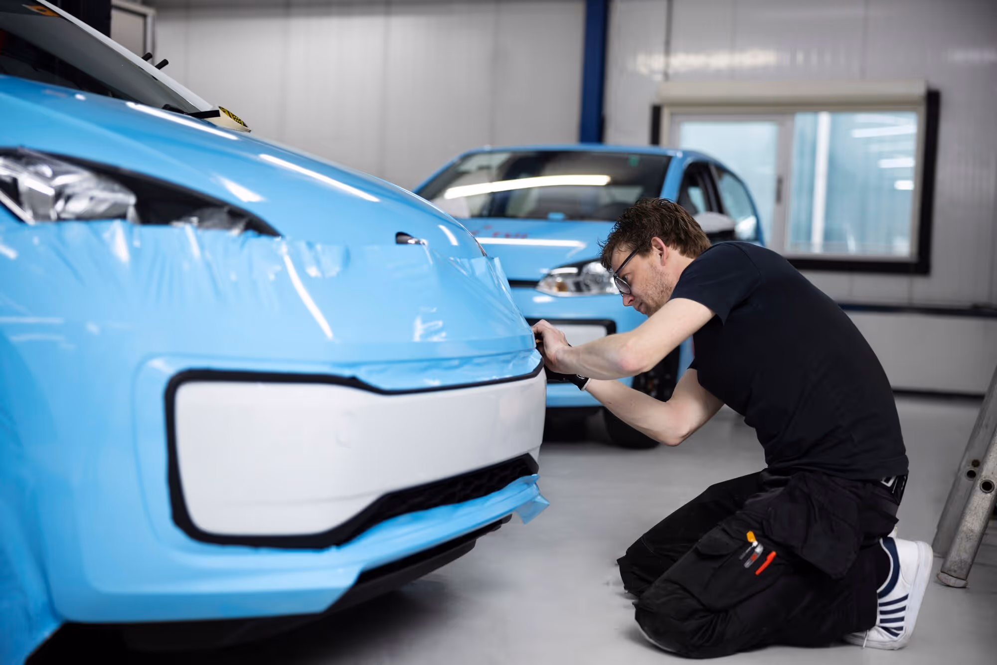 Technician wrapping a car inside a shop, illustrating Tesla safety compared to other cars