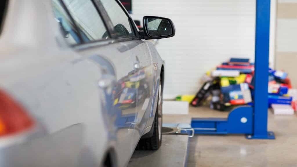 Silver car beside a two-post vehicle lift in a repair shop