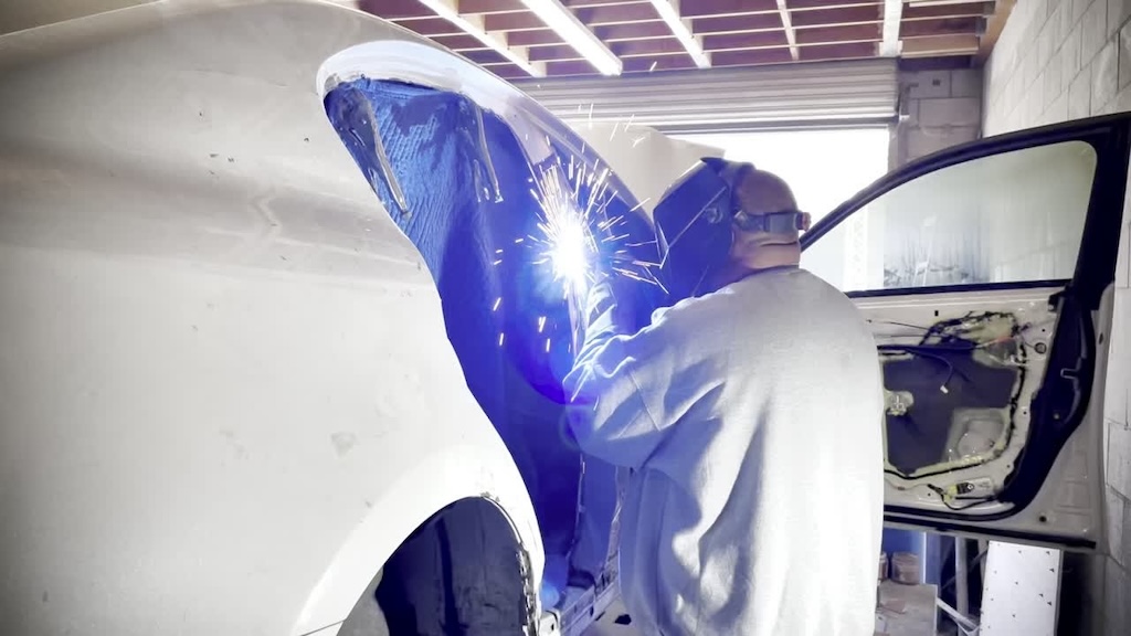 Technician welding a white car body panel during structural repair