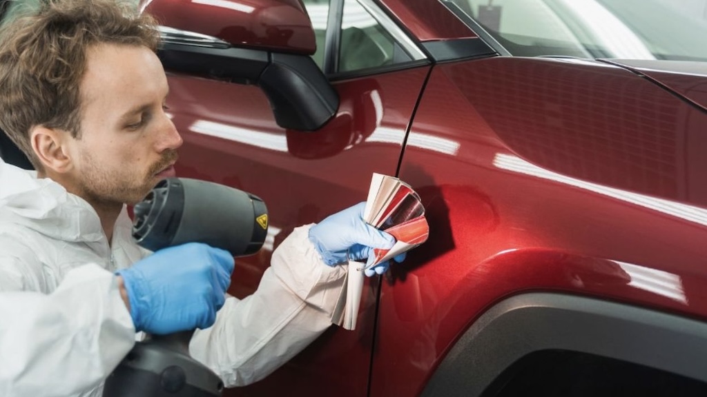 Technician comparing paint color swatches to a red car door