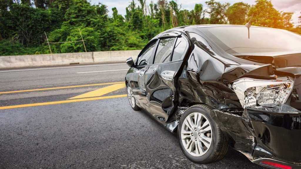 Black sedan with severe side and rear collision damage on a road