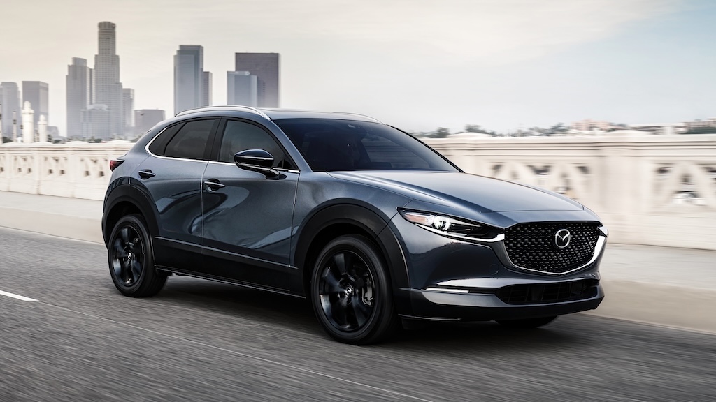 Gray Mazda CX-30 driving past a city skyline
