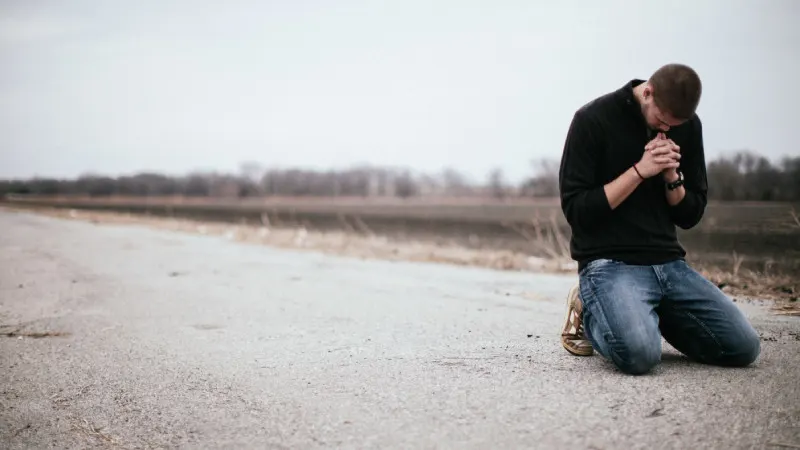 Man praying on his knees on an open road