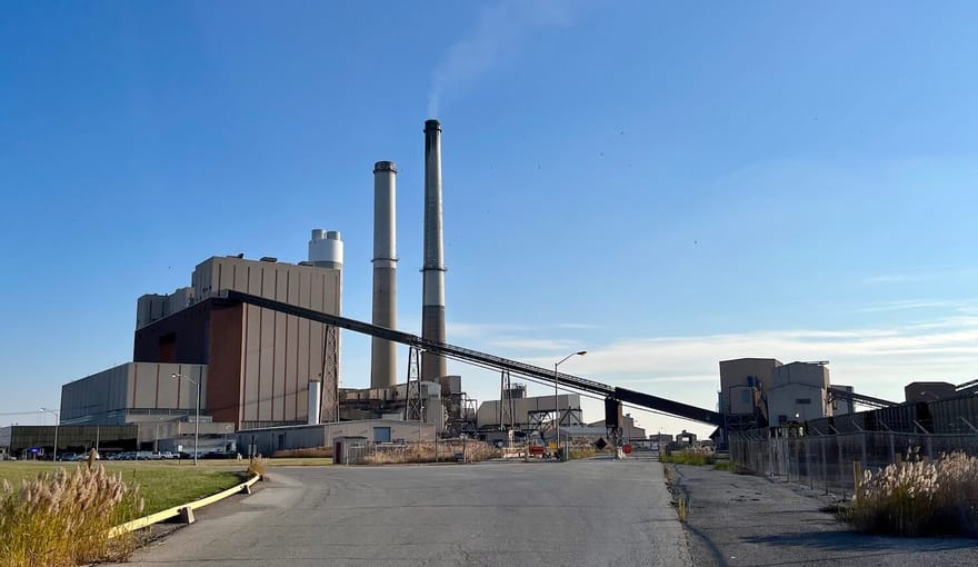 Coal plant from the roadway leading to it on a mostly clear blue day.
