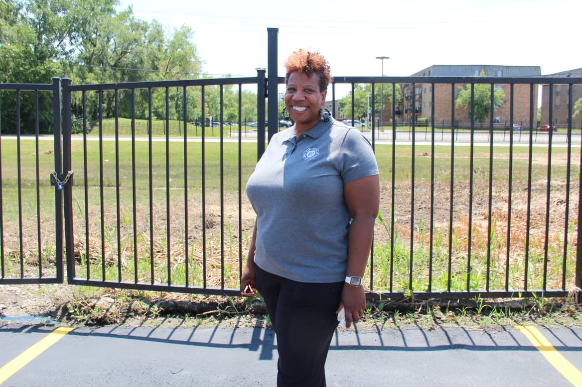 A woman in gray short-sleeve shirt and dark pants smiles