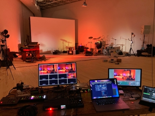 This image shows the perspective of the audio and video tech at a minimal set with warm lighting for a live streamed concert experience.