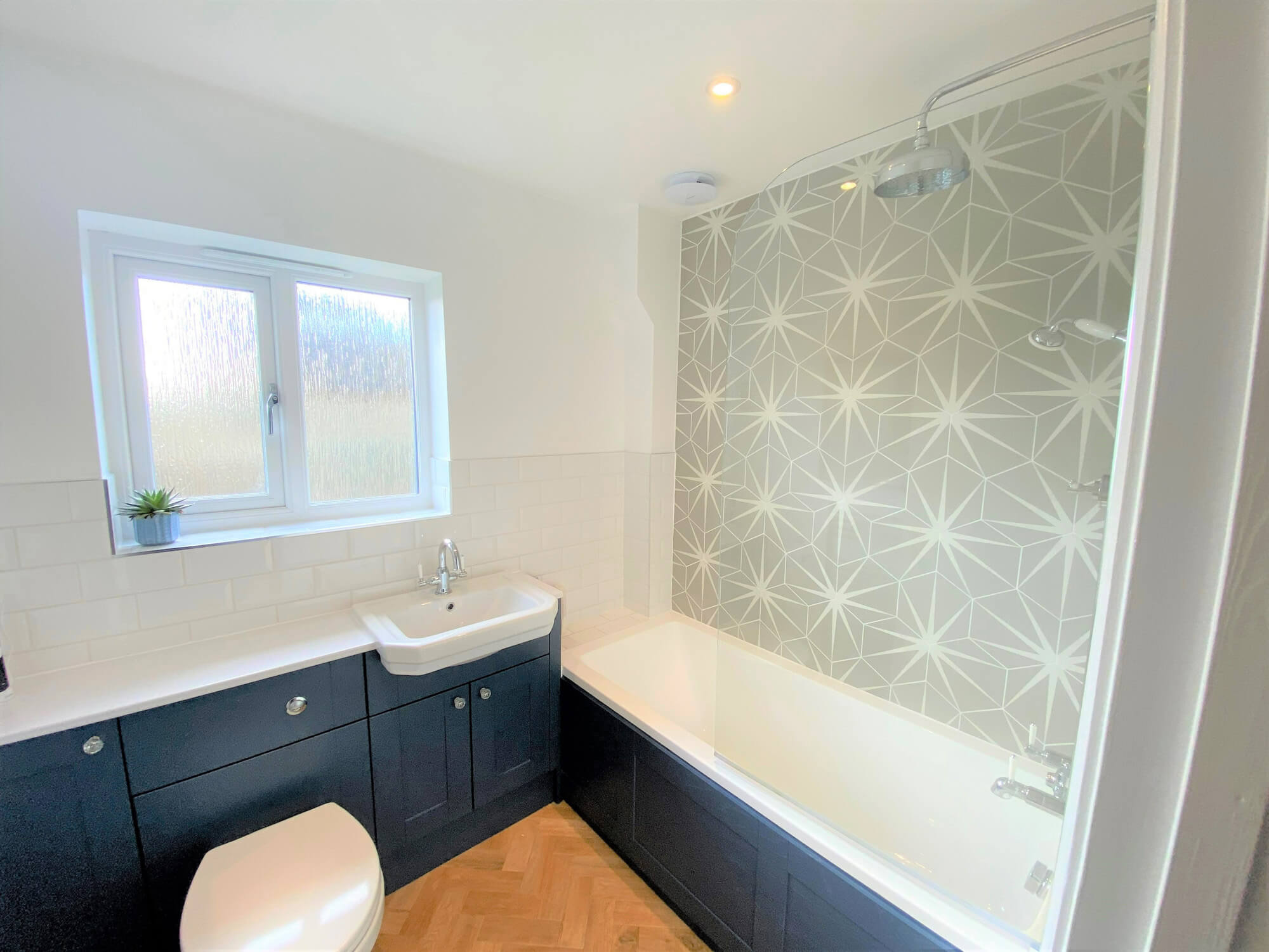 Bathroom with dark blue suite and grey coloured decorative tiles.