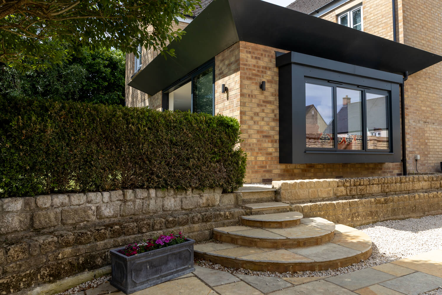 A modern brick built extension with strking aluminium features and a window seat, within a landscaped garden.
