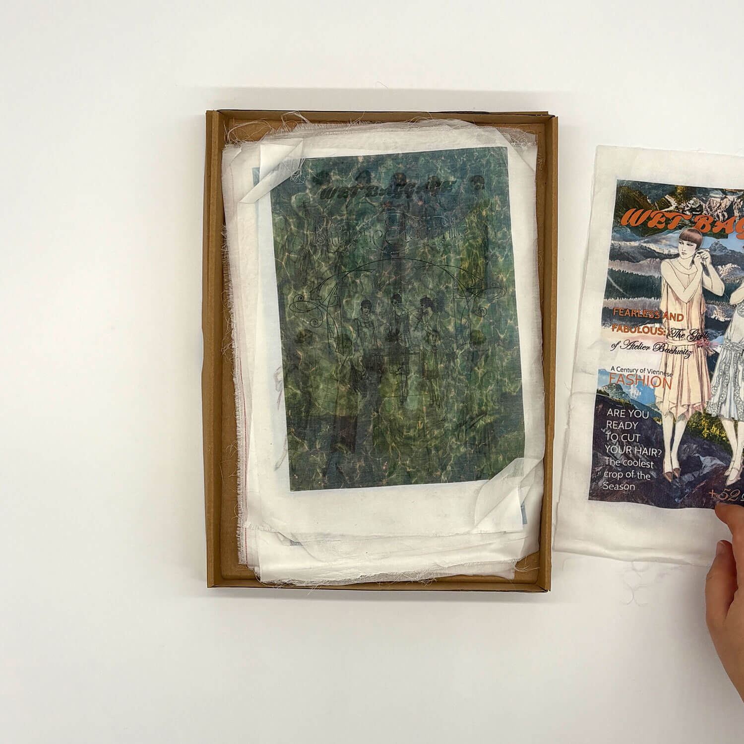 A studio photo of a designer bag and a publication printed on textile