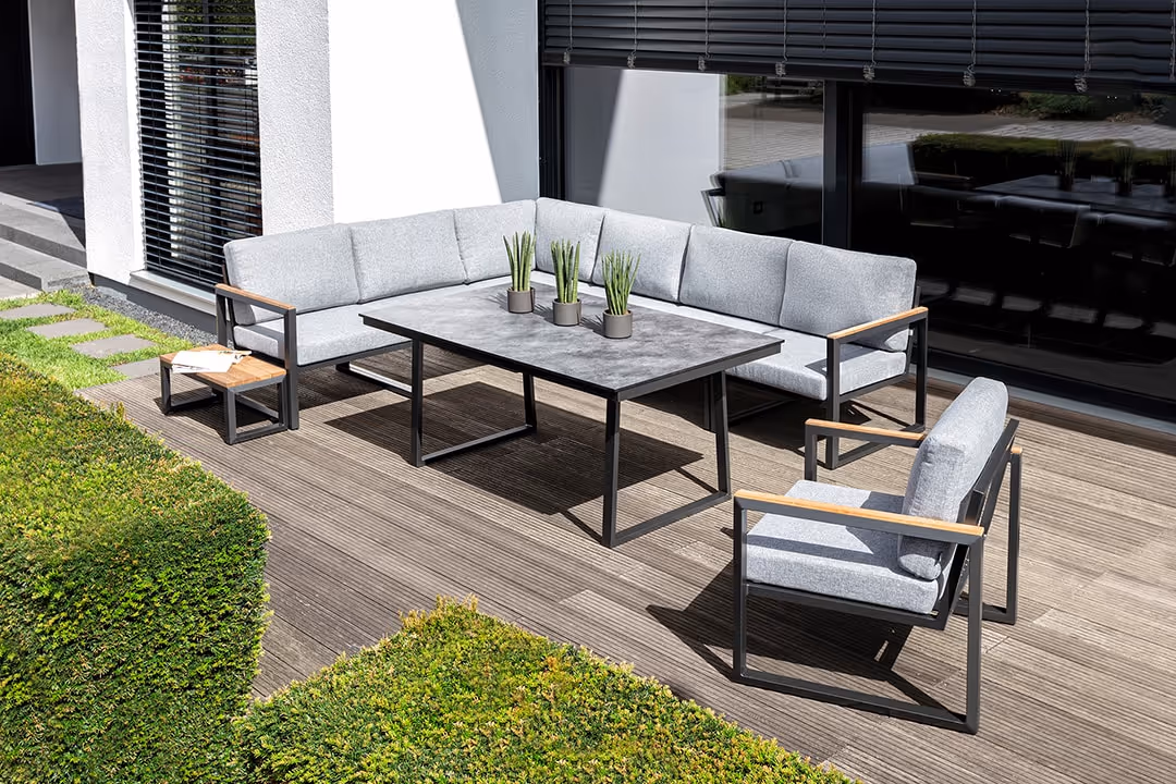 Moderne Terrasse mit grauer OCEAN SKID Ecklounge, Sesseln und einem Tisch mit drei kleinen Pflanzen.