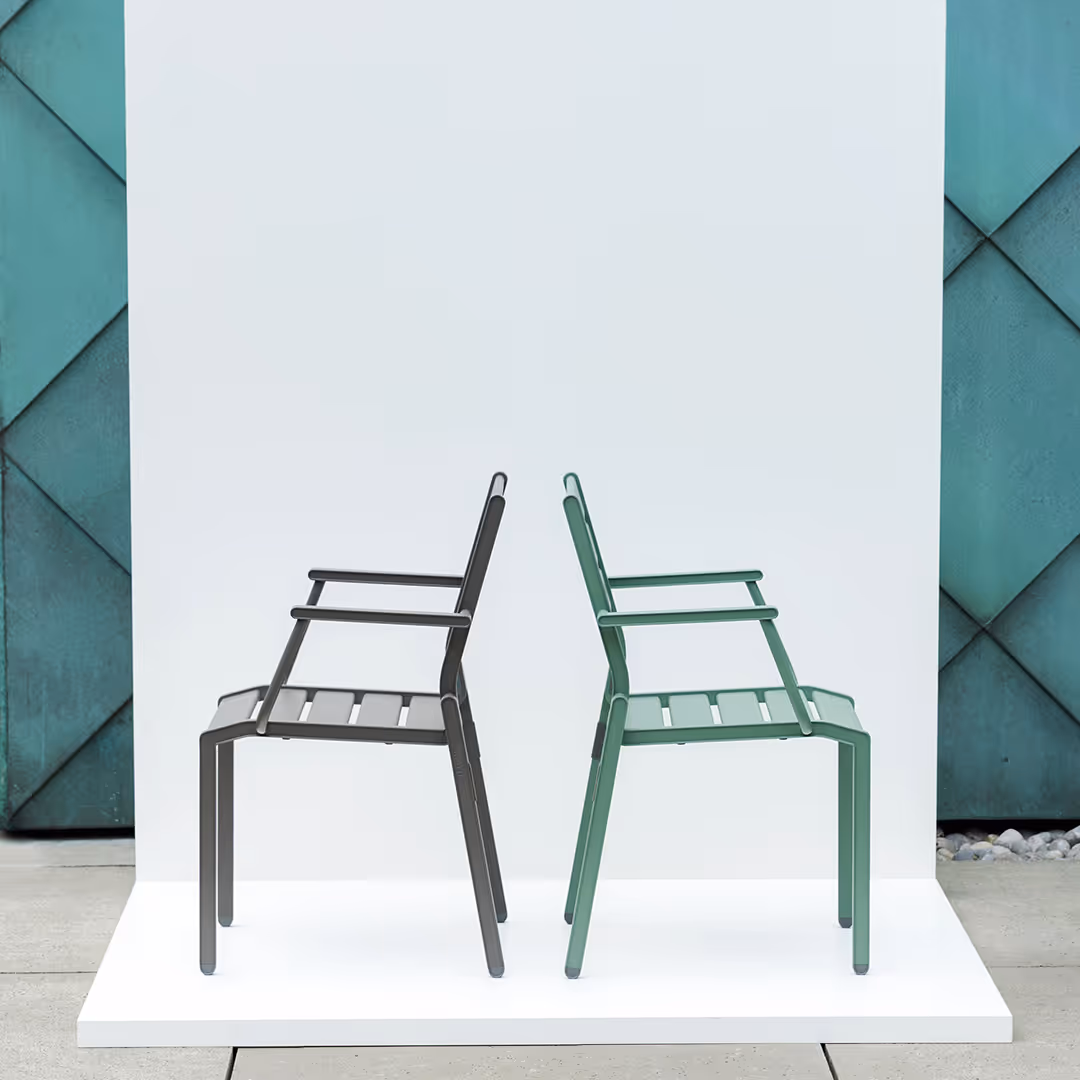 Zwei moderne Stapelstühle, einer schwarz und einer grün, nebeneinander auf einer weißen Plattform vor einer weißen und grünen Hintergrundwand.