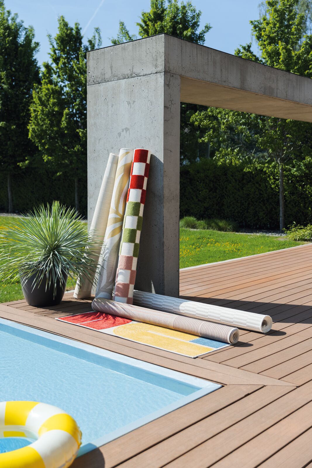 OUTDOORTEPPICHE von KETTLER gerollt an eine Wand angelehnt sowie einer geöffnet vor einem Pool.