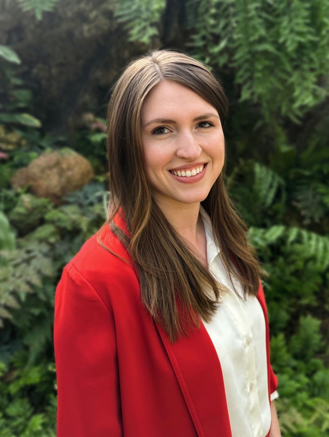A portrait of Dr. Zoie Sheets smiling. A woman with brown hair a light complexion wearing a white shirt and red cardigan.