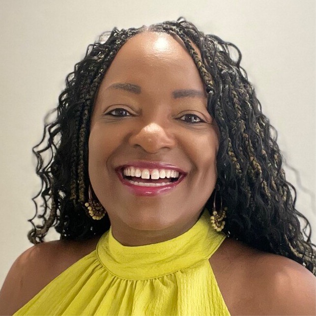 A Black woman with a medium to dark skin tone smiles brightly at the camera. She is wearing a sleeveless yellow top with a high collar, braids, and gold earrings.